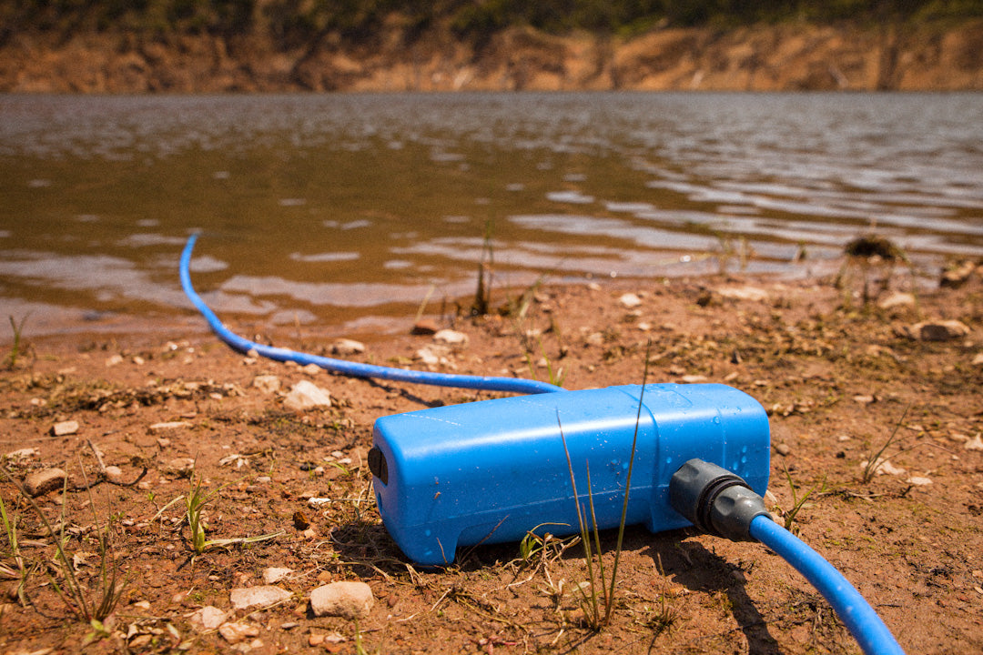 Blue 12V pump on a lakeshore with its intake hose running into the water