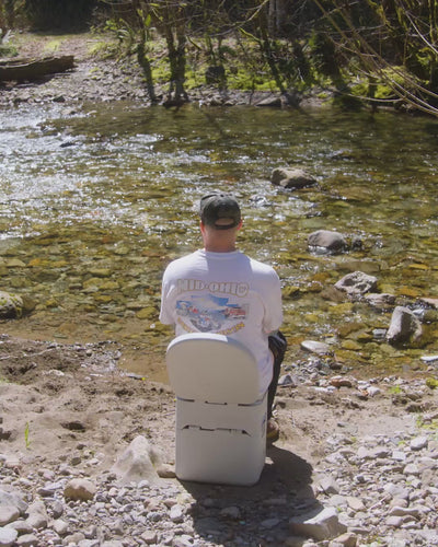 Person sitting on a portable toilet outdoors reading a book