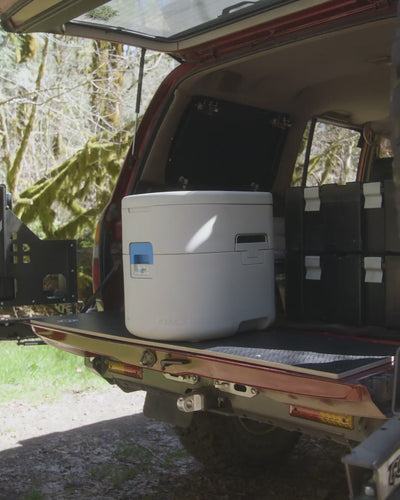 GottaGo sitting closed on a vehicle's rear slide-out tray with the tailgate open and forest behind.