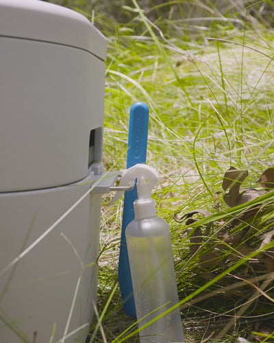 Spray bottle and blue GottaGo scraper hooked onto the side of the GottaGo out in the grass.